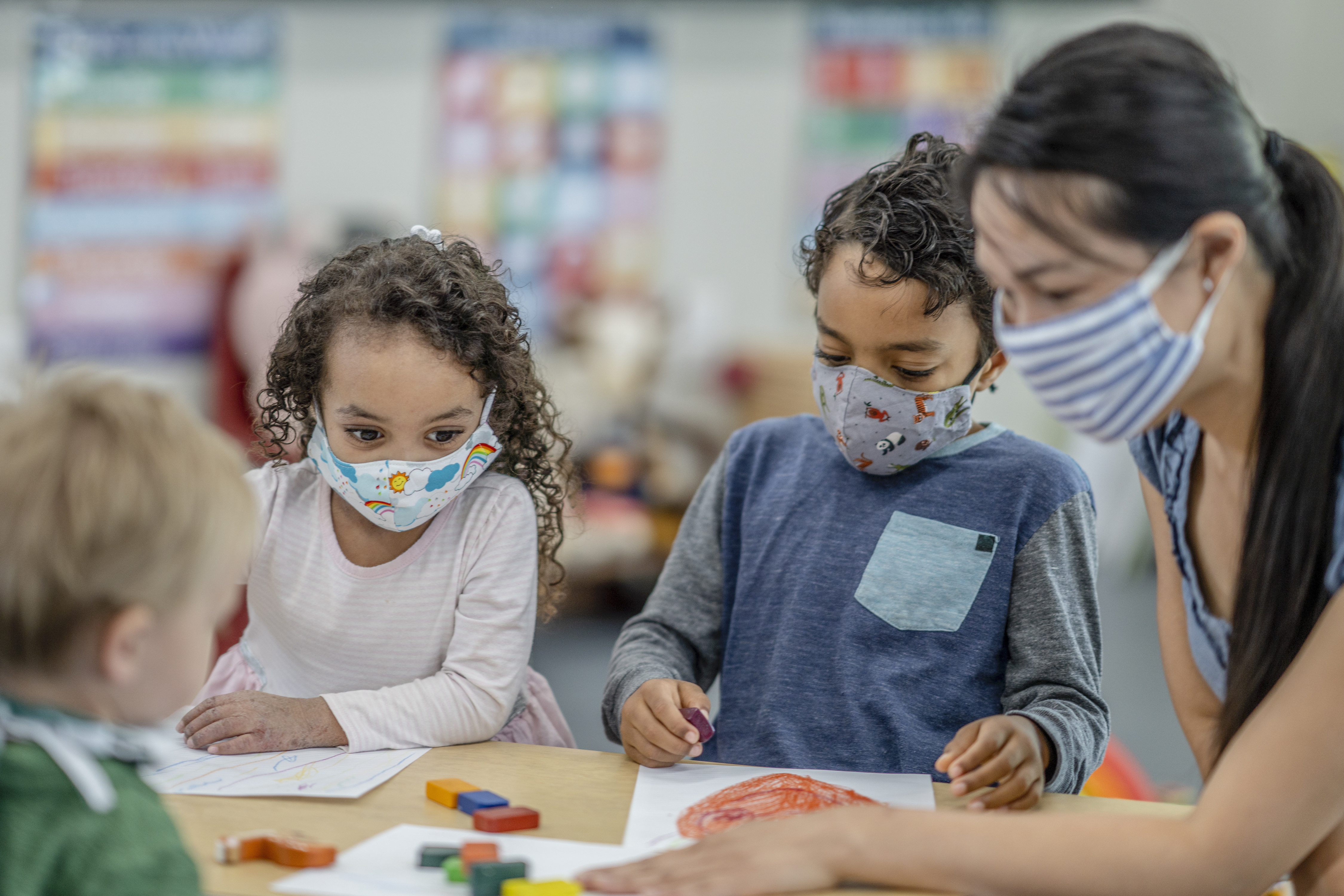 Multi-ethnic group of children colouring at a table while wearing protective face masks to avoid the transfer of germs.